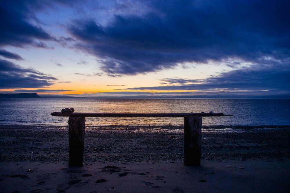 Wooden bench on sandy beach at sunset with ocean and cloudy sky, WA, USA.