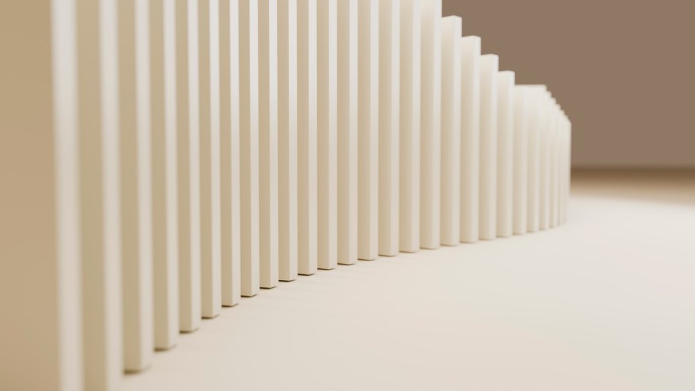 Row of beige wooden dominoes stands in a curved line casting shadows on a smooth surface in a minimalist setting.