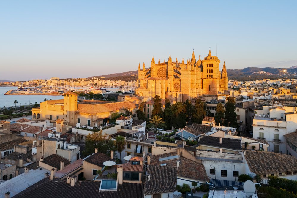Cathedral of Palma de Mallorca illuminated by sunset light overlooking rooftops, harbor, and mountains, Landscape, Lifestyle, Balearic Islands, Spain.