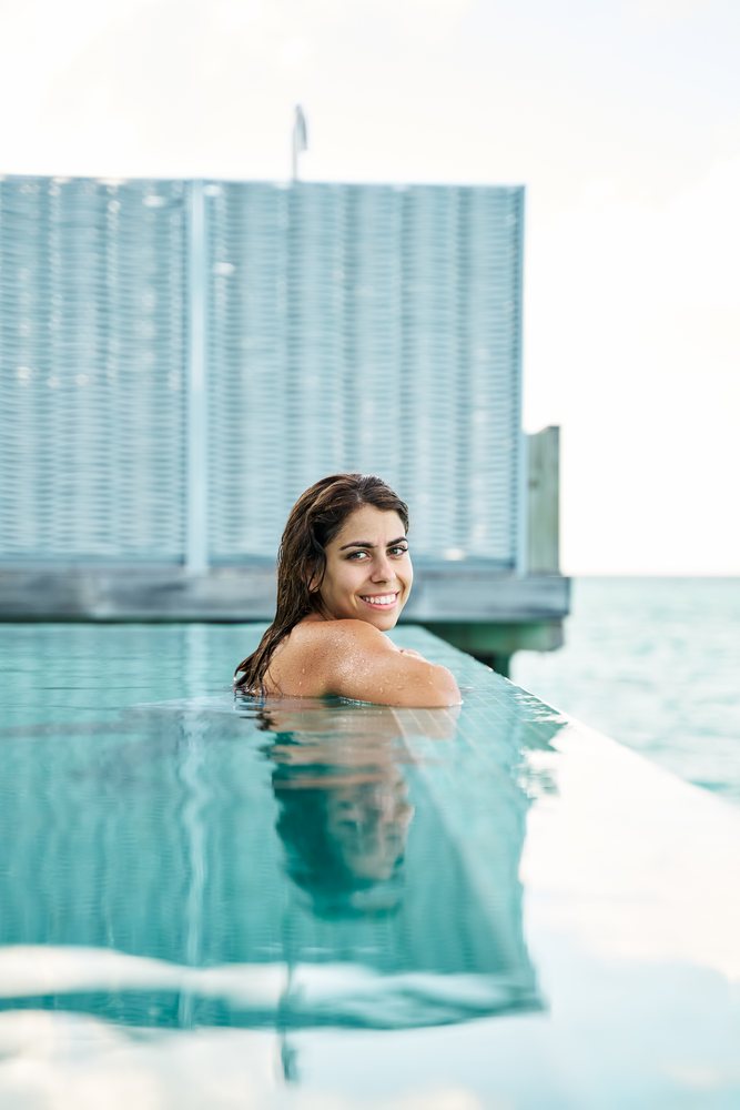 A white woman relaxes and smiles in an infinity pool with ocean views