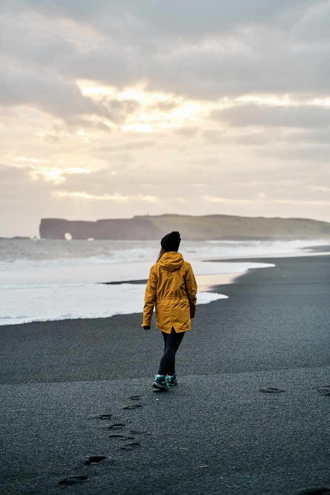 White Person walking on a black sand beach by the ocean in a beach