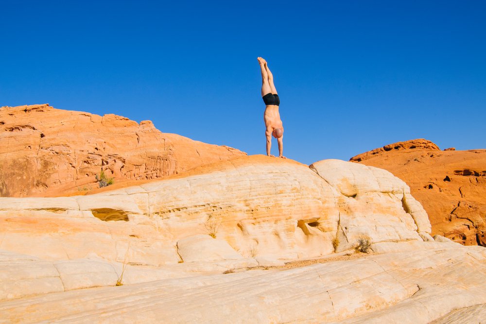 Person performs a handstand on a desert rock formation under a clear blue sky, yoga, acrobatics, USA.