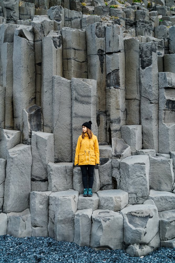 A white woman stands on basalt columns showcasing Iceland's striking