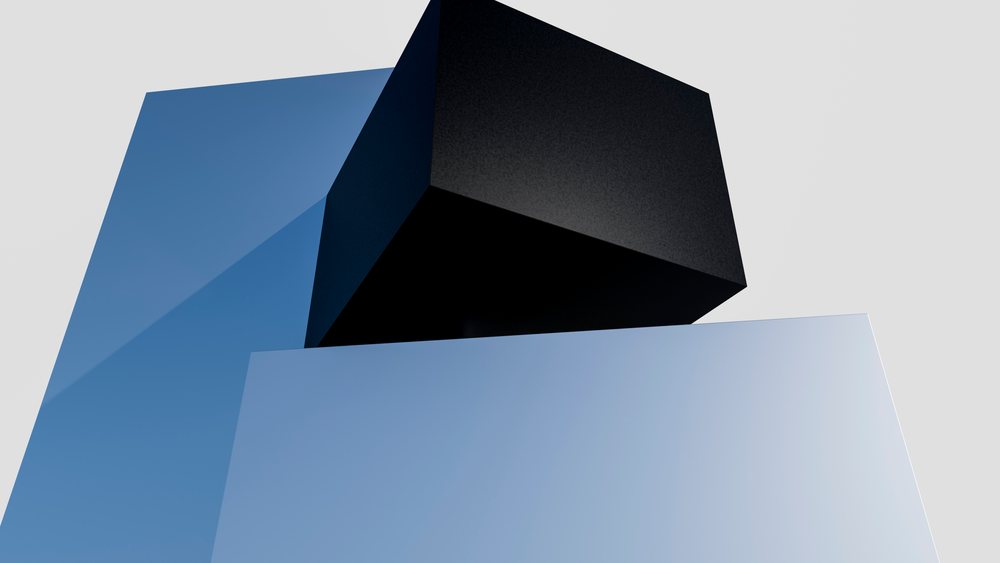 Two vertically stacked cubes, with a matte black cube on top and a glossy blue cube below, form a minimalist geometric sculpture in a plain light gray setting.