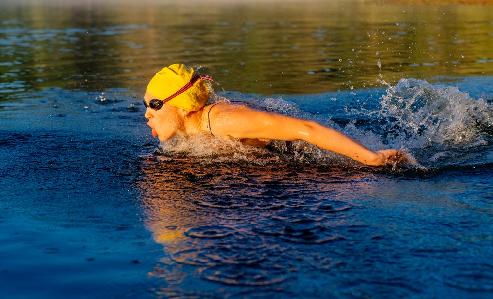 Swimmer wearing a yellow swim cap and goggles performing breaststroke in open water during training, USA.