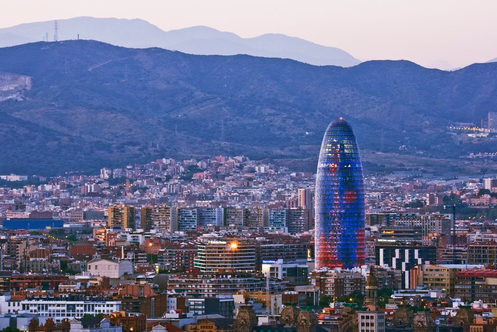 Agbar Tower illuminated at twilight dominates Barcelona's urban skyline with mountains behind, Catalunya, Spain.