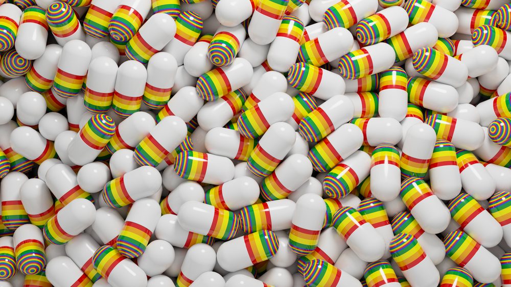 Close-up of white medication capsules with rainbow stripes piled together.