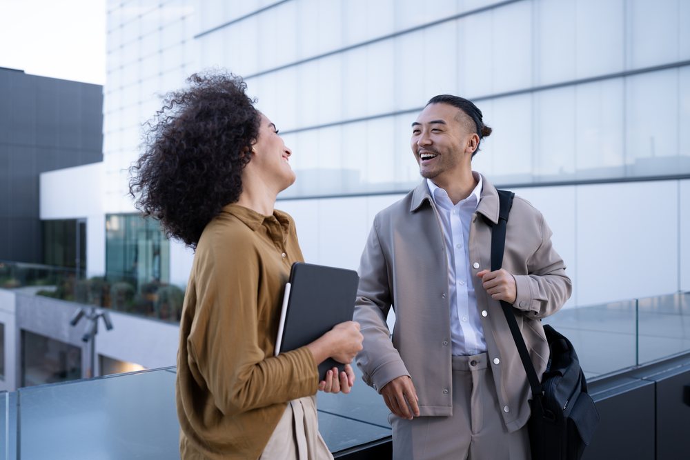 Two colleagues laugh and converse on an outdoor terrace beside a modern building, Madrid, Spain.