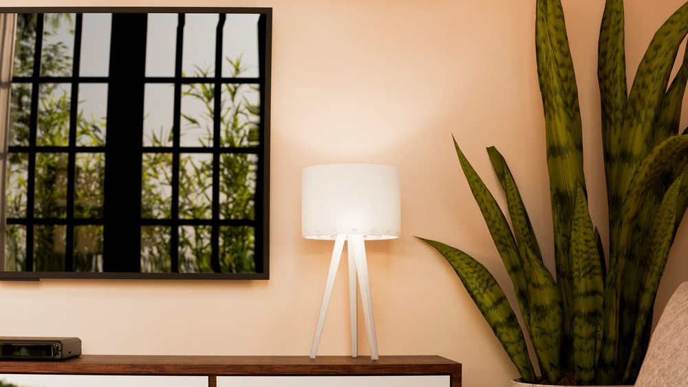 White three-legged table lamp with cylindrical shade on wooden cabinet beside potted snake plant in living room interior with window reflection on TV screen.