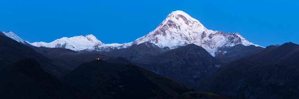 Gergeti Trinity Church illuminated at Dawn below snow-capped Mount Kazbegi, Georgia.