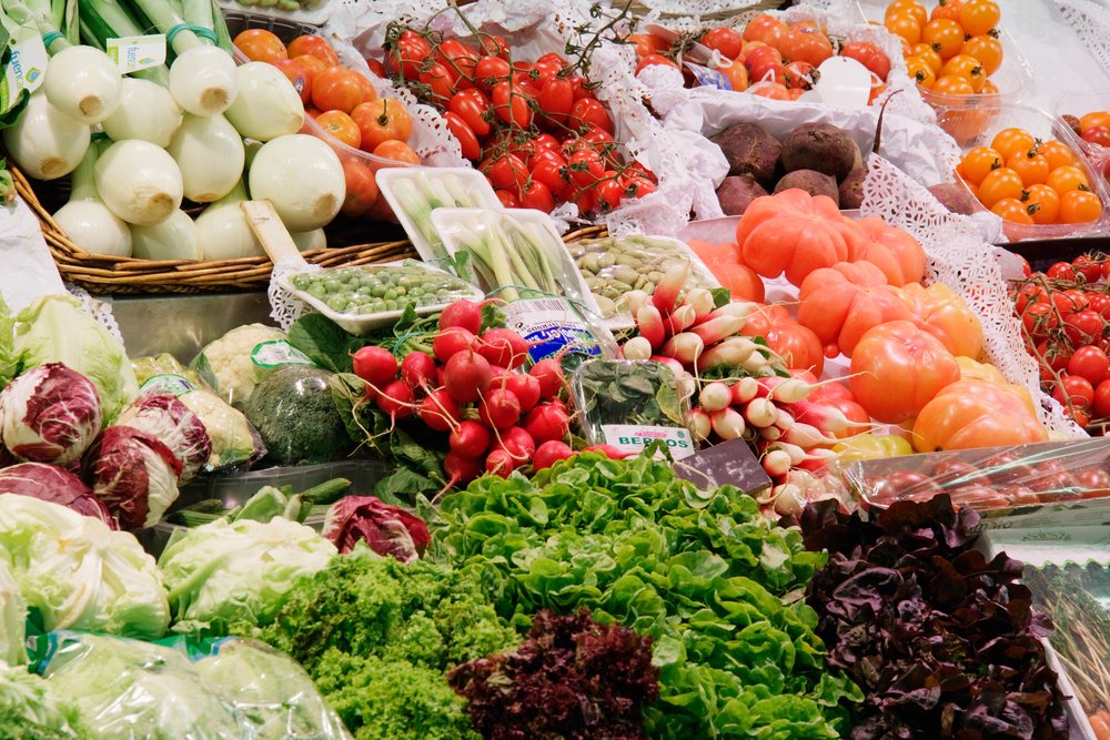 Fresh vegetables including onions, tomatoes, radishes, white radishes, beetroots, lettuce, broccoli, cauliflower, green peas, and broad beans displayed at Santa Catarina Market, Catalunya, Spain.