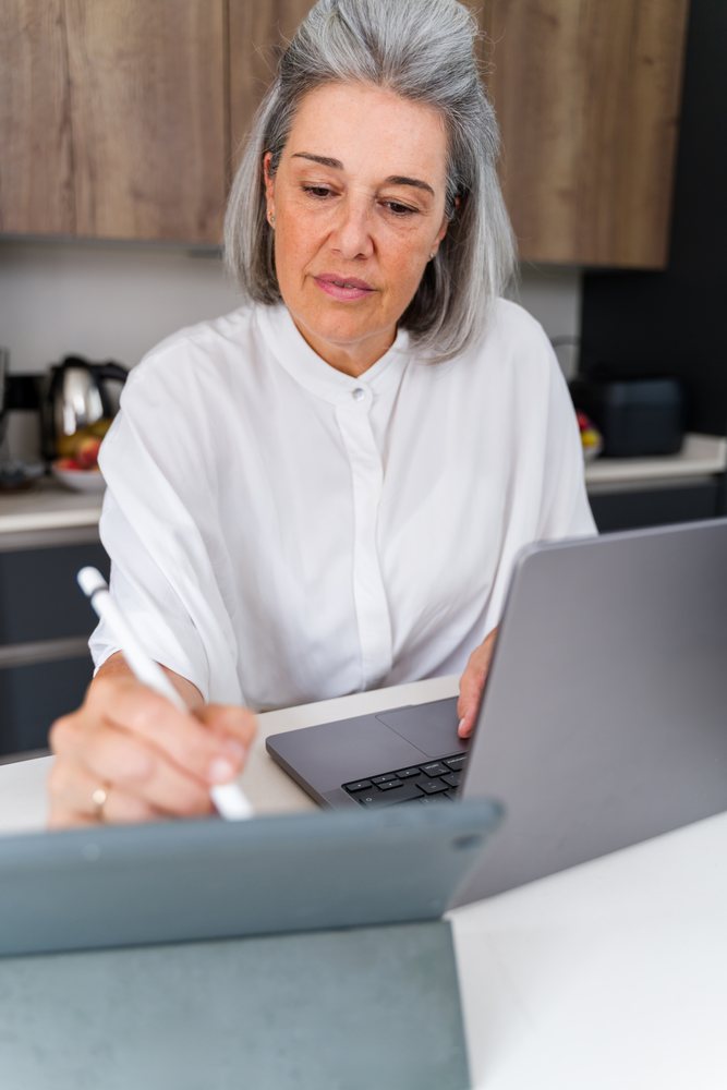 Woman using a digital pen and laptop at home, Spain.