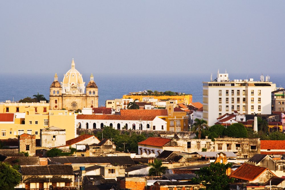 Historic Iglesia de San Pedro Claver with yellow dome and twin towers overlooking rooftops and the ocean, Colombia under a clear sky, Cartagena.