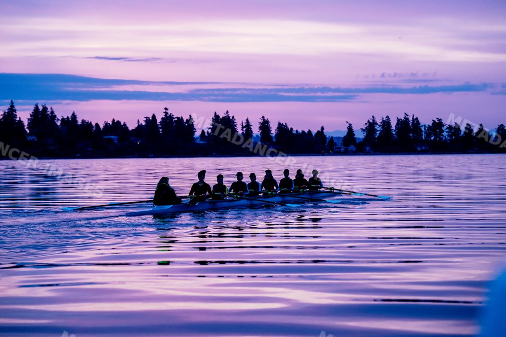 A rowing team trains together on calm lake water at sunset