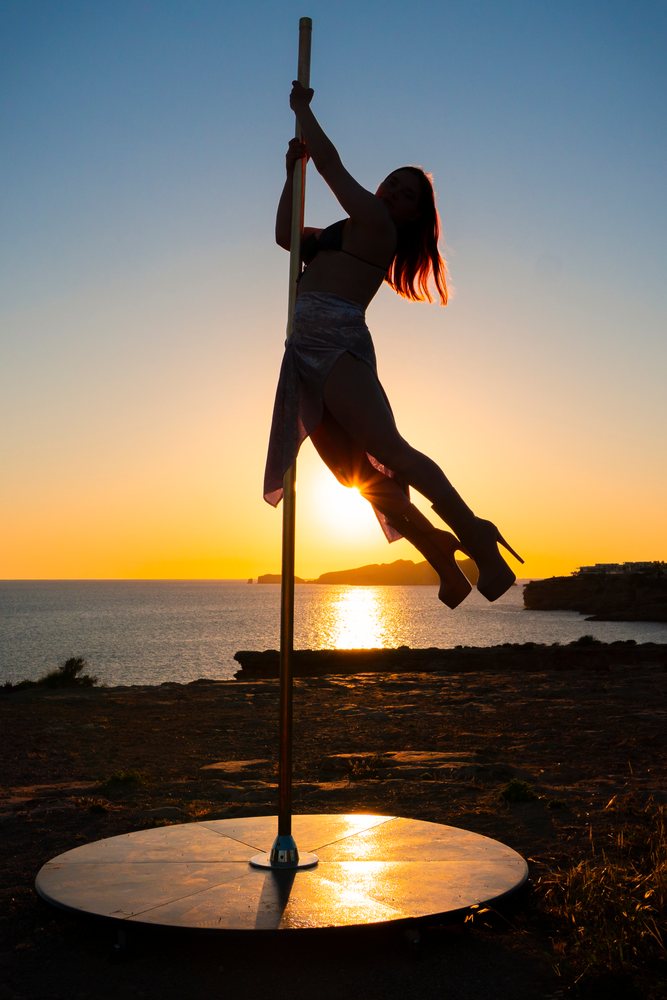 Silhouette of a woman performing pole dance at sunset by the rocky sea coast, Ibiza, Spain.