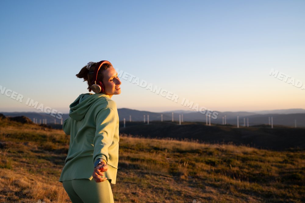 A white woman enjoys music outdoors near wind turbines in Galicia