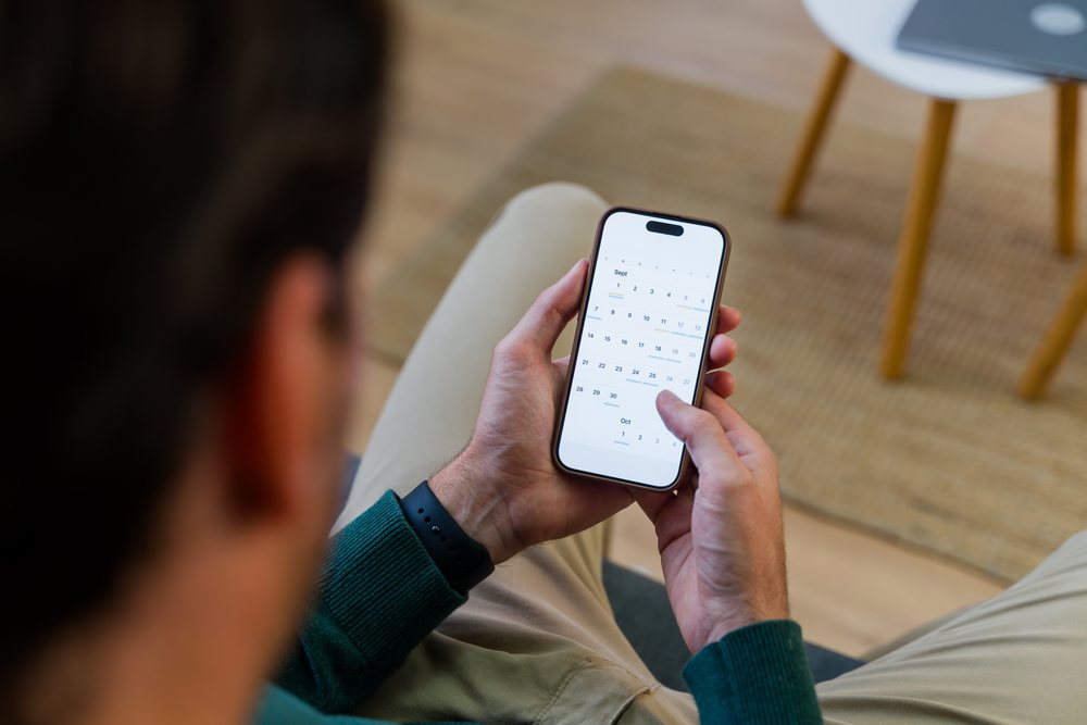 Man sitting indoors using a smartphone to interact with a calendar app in a modern home environment, Spain.