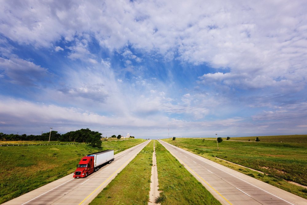 Semi truck drives along the multi-lane Interstate 40 highway bordered by green grass under a partly cloudy sky, Texas, USA.