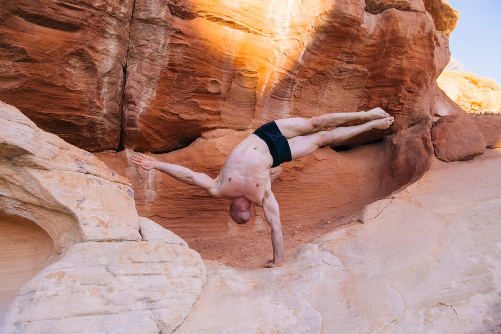 Man performs a handstand yoga pose on red rock formations outdoors, USA.