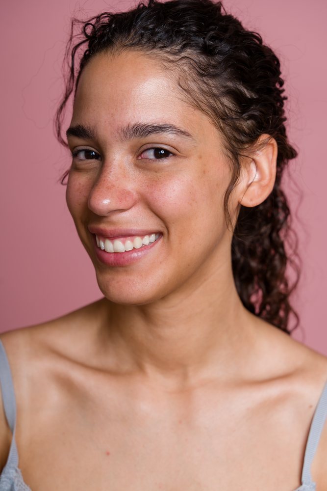 Head and shoulders portrait of a smiling woman with curly hair against a pink background in a studio, beauty shoot, Spain.