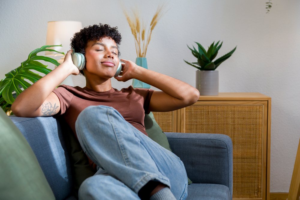 Young woman wearing headphones relaxes on a sofa at home.