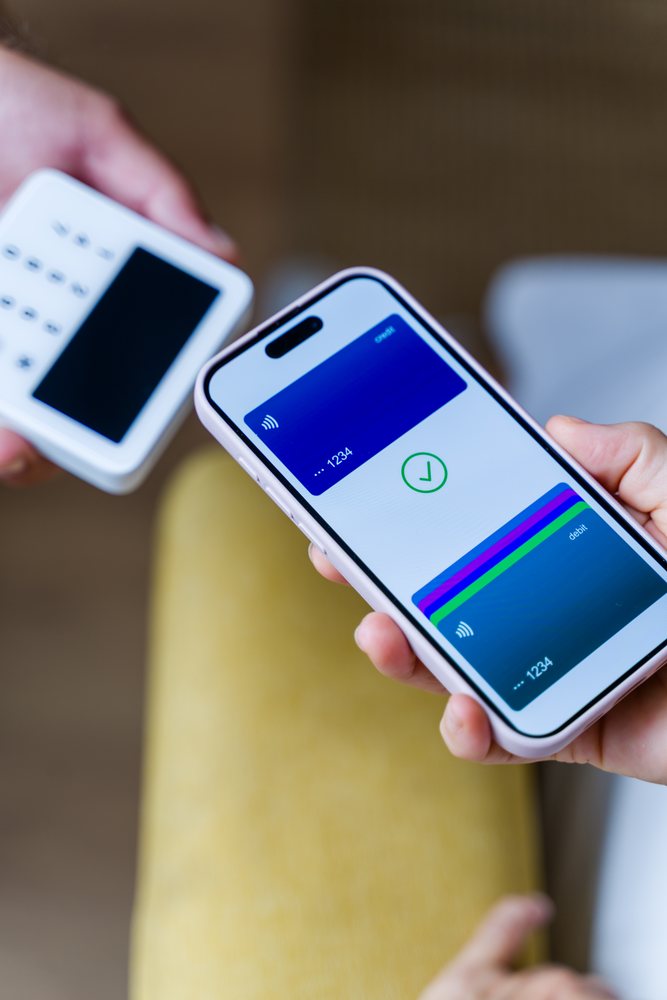 Smartphone held in hand shows contactless payment confirmation near a payment terminal, Spain.