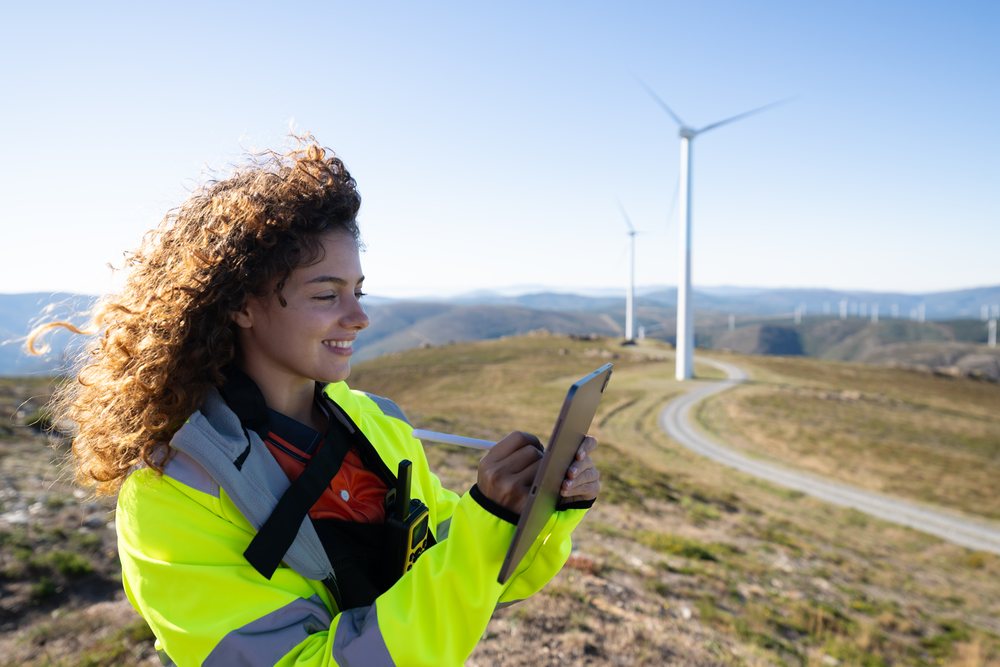 Smiling woman engineer in a high visibility jacket uses a tablet at a wind farm, sustainability, renewable energy, Galicia, Spain.