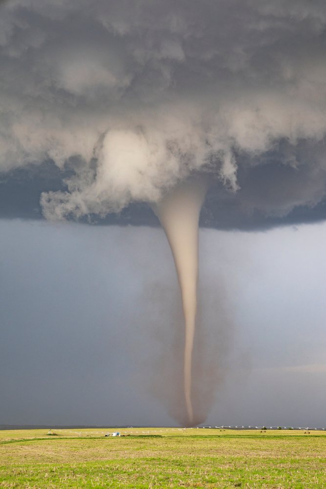 Fully Condensed Tornado funnel descends from dark storm clouds onto green irrigated farmland, within the Great Plains Tornado Alley, Dickens, Nebraska, USA.