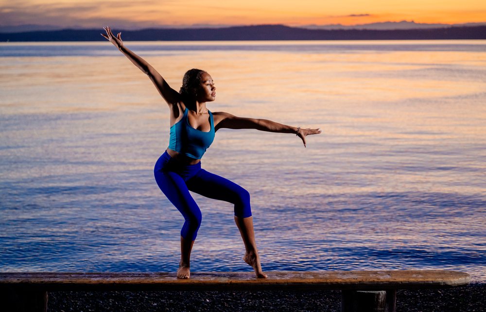 Woman balancing in a yoga pose on a wooden beam at sunset by a lake, USA.
