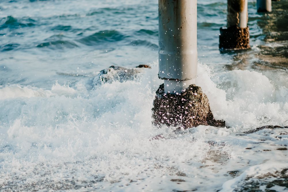 Waves crash against concrete pillars of a pier in the ocean, creating water splashes and sea foam, Spain.