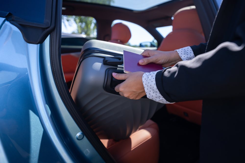 Businesswoman placing a suitcase inside a car while holding a passport during travel, Business Travel, Luggage, Spain.
