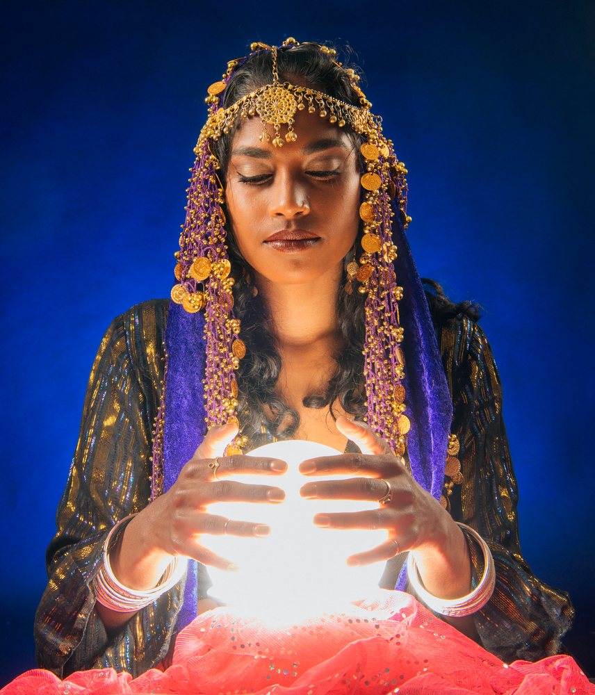 A fortune teller holding a glowing crystal ball with eyes closed in a dark room in the, USA.