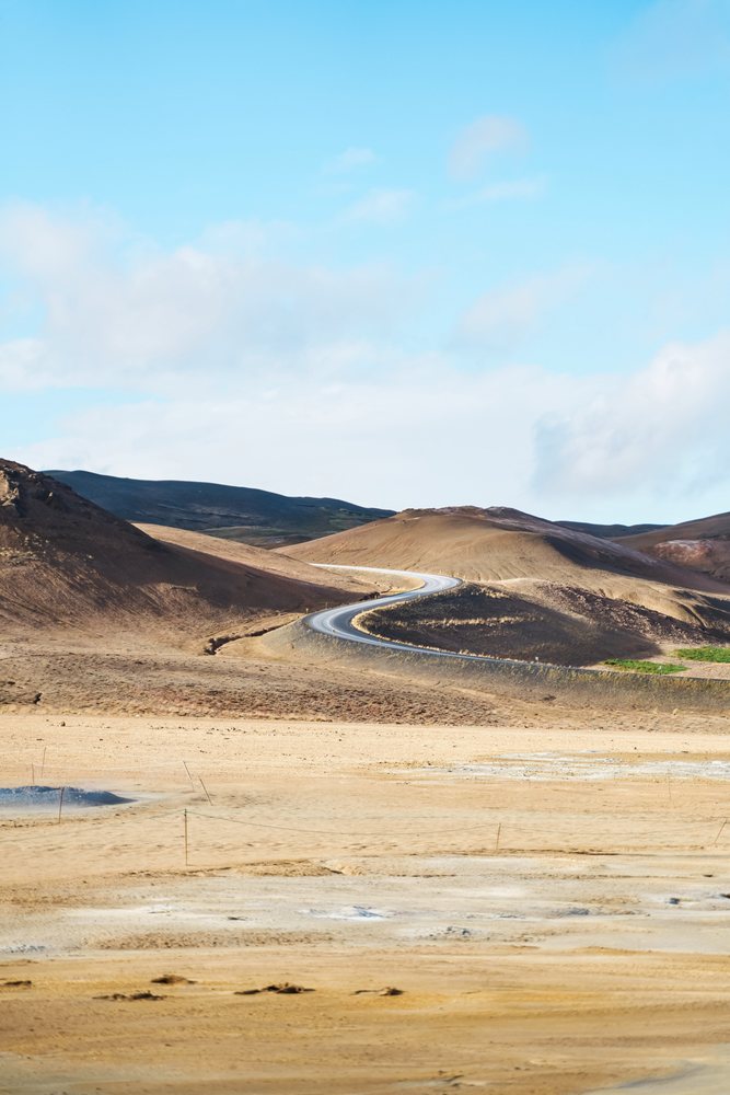 A winding road curves through barren brown hills under a blue sky in a dry Icelandic landscape, Iceland.