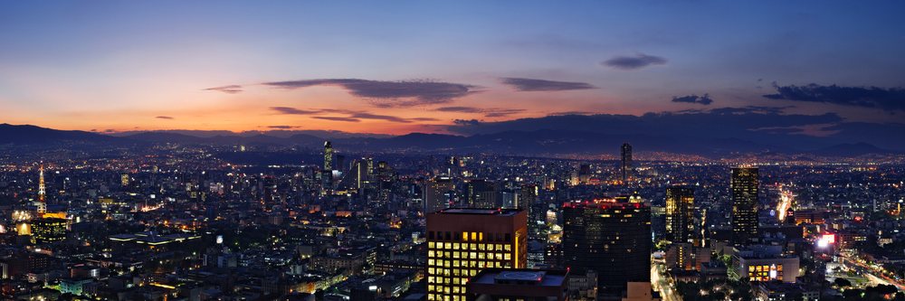 Mexico City skyline with illuminated buildings and colorful sunset sky backed by mountains, Dusk.