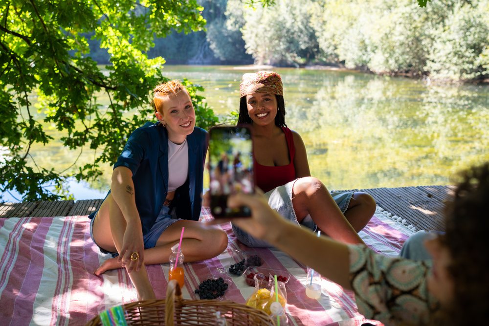 Two women enjoy a picnic by the lake sitting on a striped blanket, Spain.