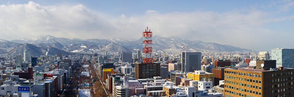 City skyline of Sapporo with snow-covered mountains in the background under a partly cloudy winter sky, Hokkaido, Japan.