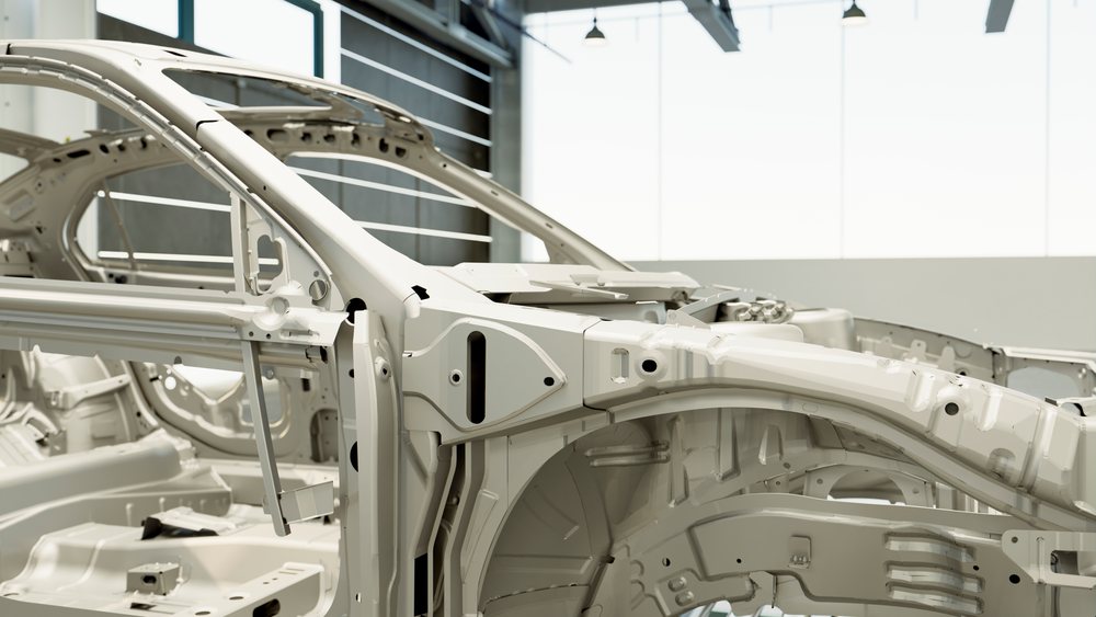 Metal car frames in an industrial factory undergoing chassis assembly during automobile manufacturing.