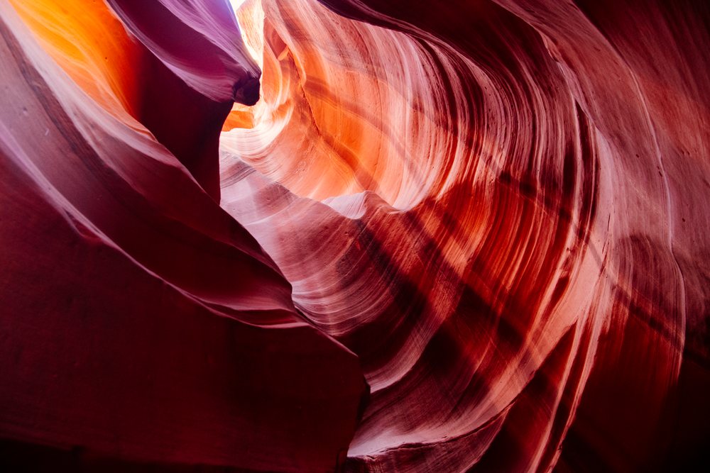 Natural light illuminates orange and purple curved sandstone walls inside Antelope Canyon, Navajo Land, Arizona, USA.