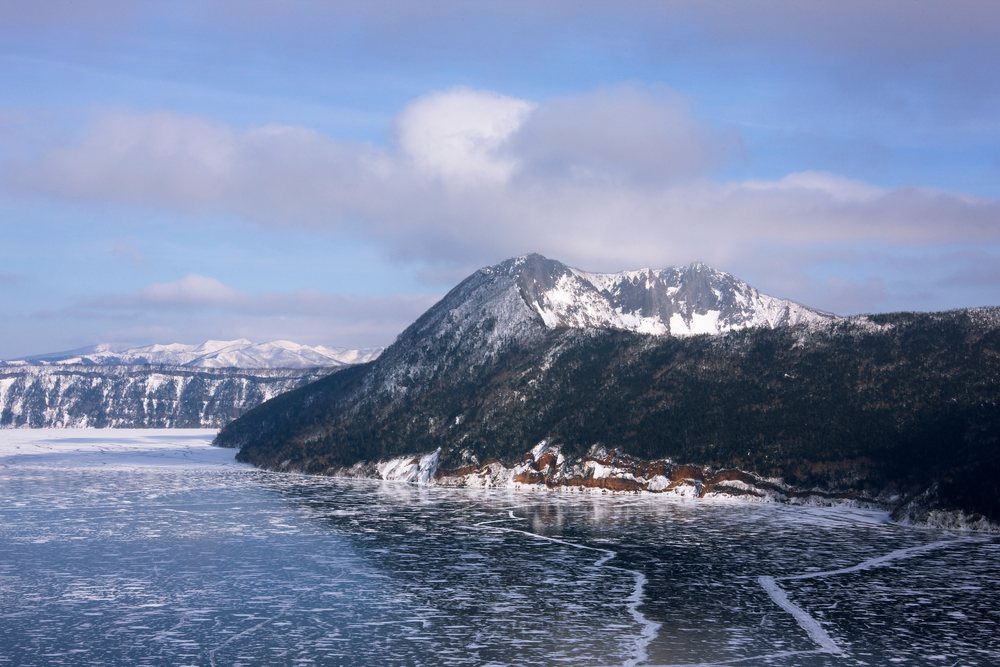Frozen Lake Mashu with snow-covered mountain and icy surface showing visible cracks, Winter, Akan National.