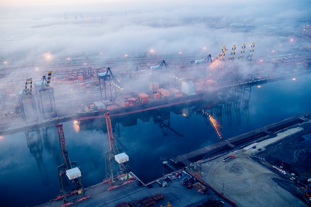 Container ship docked at cargo terminal with port cranes and shipping containers partially covered in fog at the, Port of Long Beach, CA, USA.
