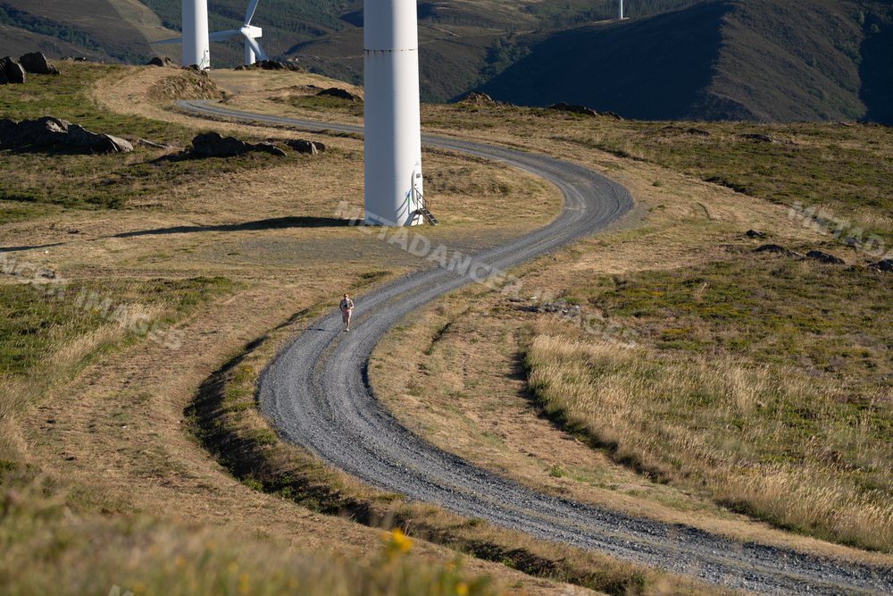 A white woman trail runs along a winding path beside wind turbines