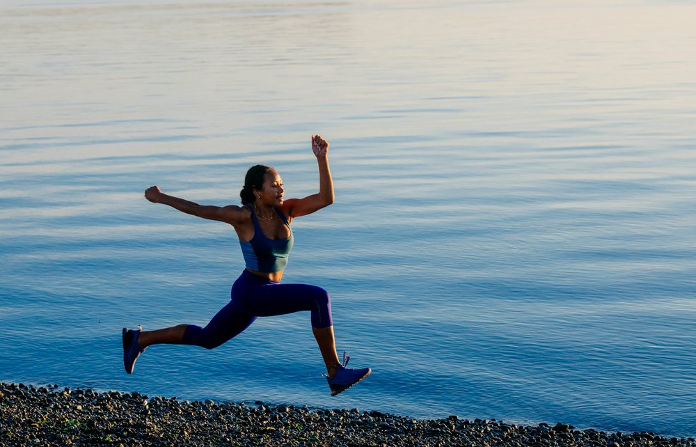 Woman energetically jumping along the pebbled shoreline of a calm lake, yoga, acrobatics, USA.