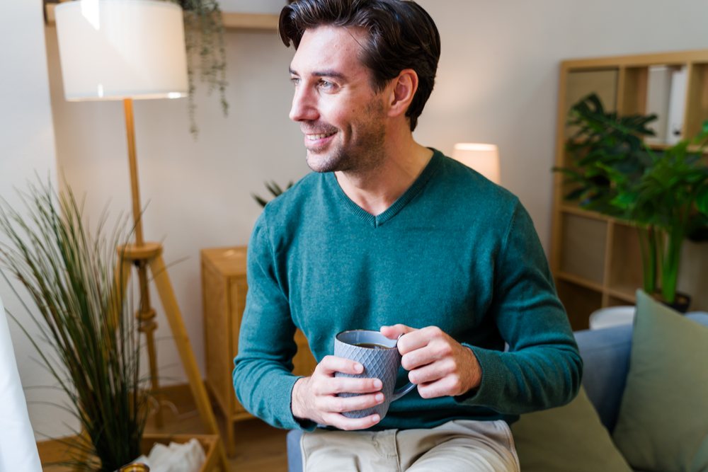 Man sitting indoors in a living room holding a mug and smiling, Spain.