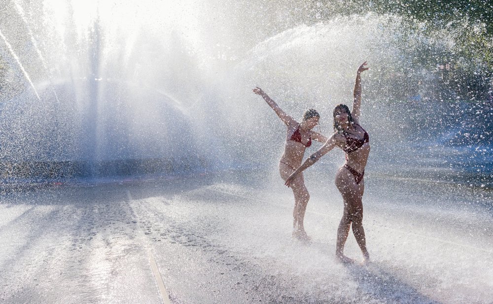 Two women dancing and playing in a public water fountain spraying water, partner, acrobatics, yoga, USA.