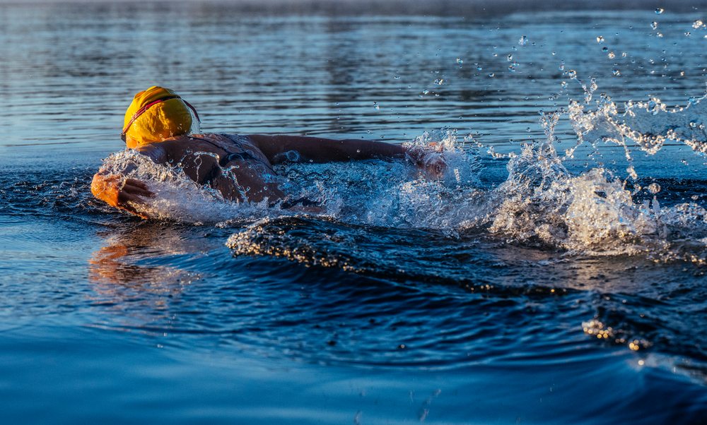 Open water swimmer wearing a yellow swim cap and goggles creating splashes while swimming outdoors, USA.