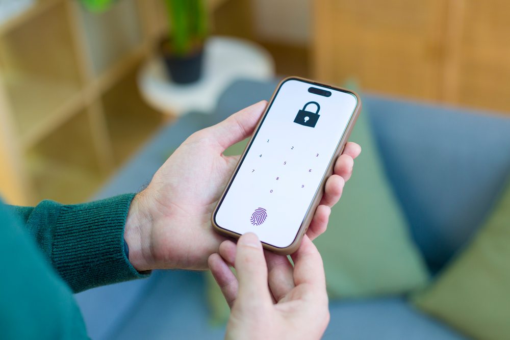 Smartphone held in one hand showing fingerprint lock screen with biometric authentication and numeric keypad indoors, technology, young adult, home.