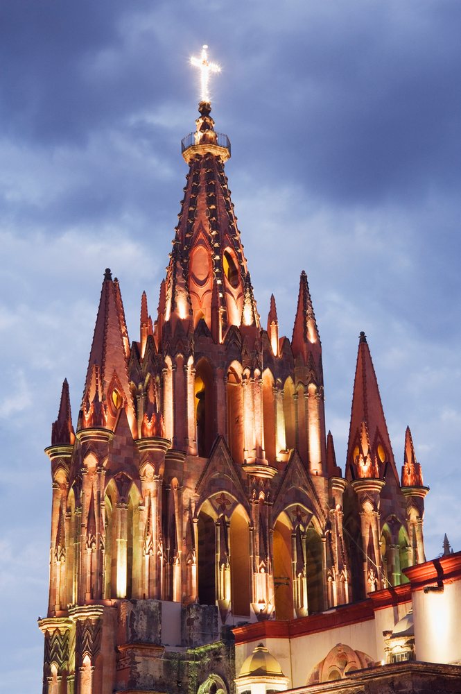 Illuminated Gothic-style church steeple with glowing cross at night, San Miguel de Allende, Mexico.