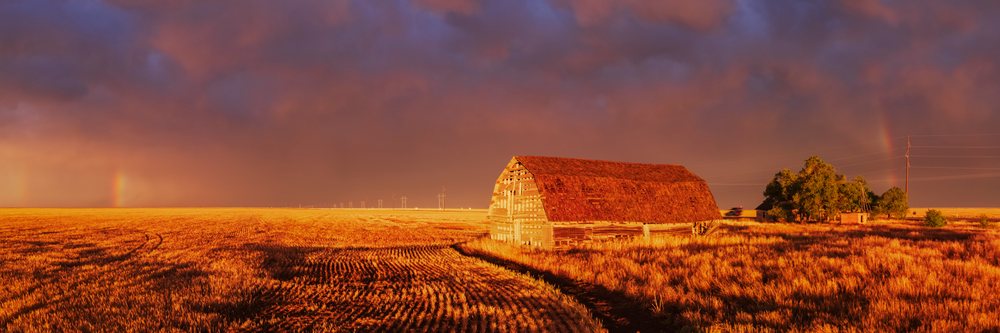 Old barn illuminated by Sunset light in a rural field, with a Rainbow visible under a dramatic sky, Storm Chasing, Weather, Environment, Eva, Oklahoma, USA.