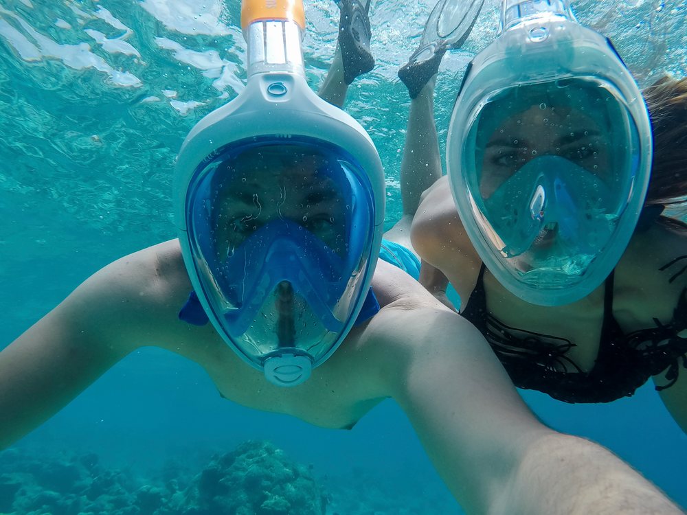A couple snorkeling underwater using full face masks above a coral reef in the, Maldives.