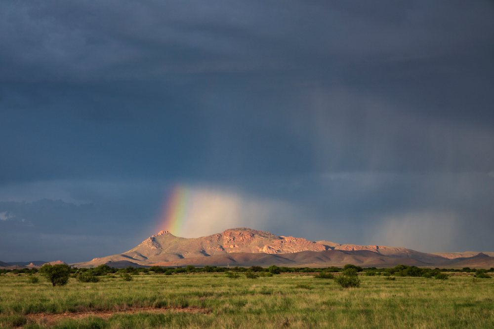 Rain Shafts and a Rainbow appear over mountains and grasslands, under stormy skies, Storm Chasing, Weather, Environmental Issues, Douglas, Arizona, USA.
